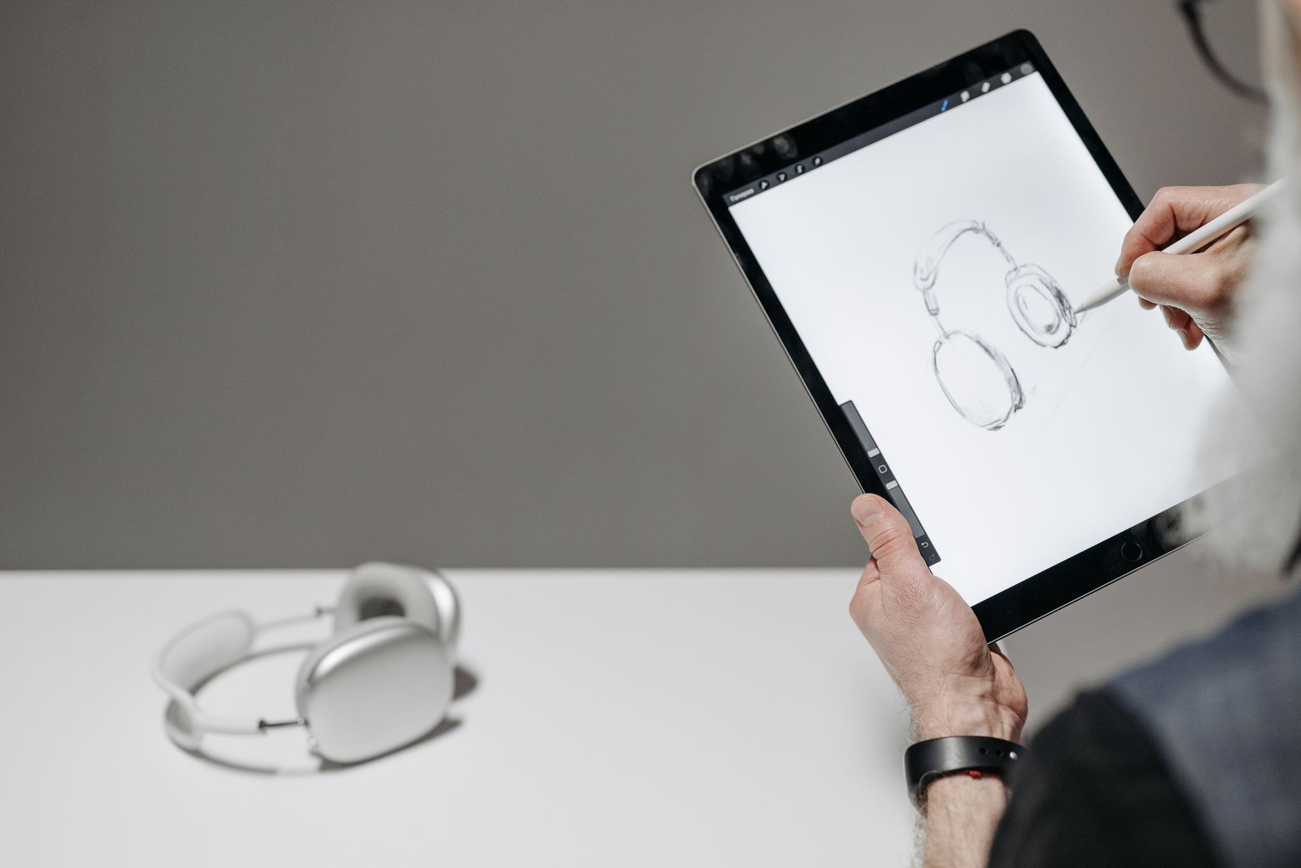 Artist sketching headphones on a tablet with stylus, creating digital art.