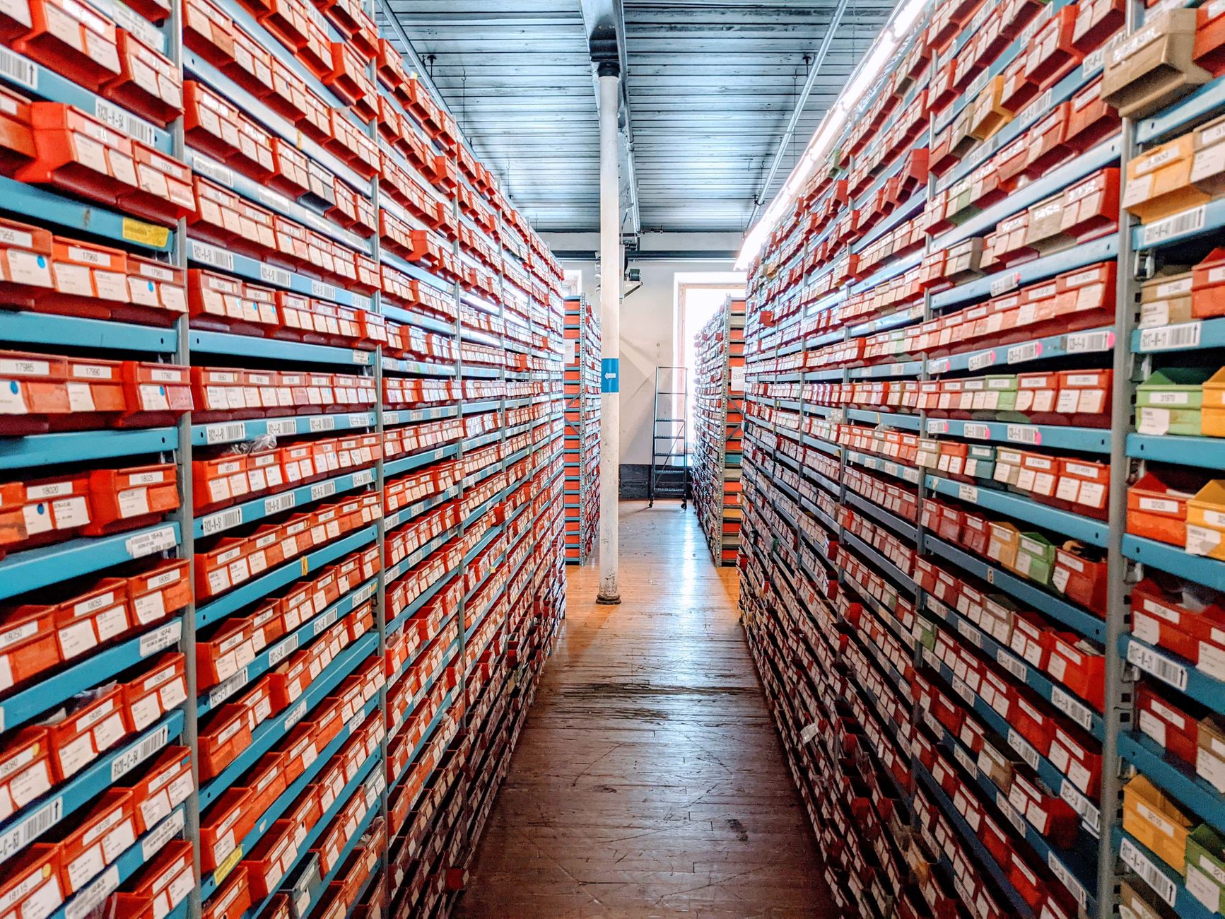 A well-organized warehouse aisle filled with red shoe boxes on shelves, showcasing efficient inventory storage.