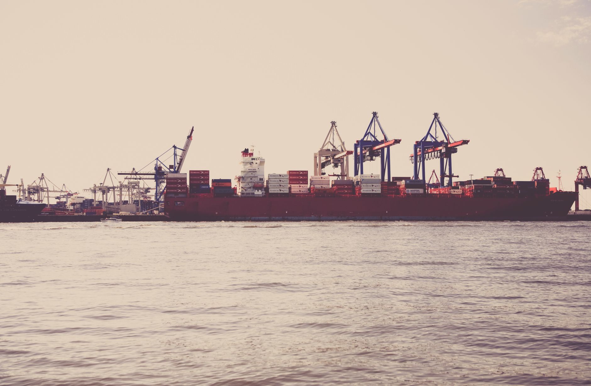 A cargo ship loaded with containers docked at a seaport under clear skies.